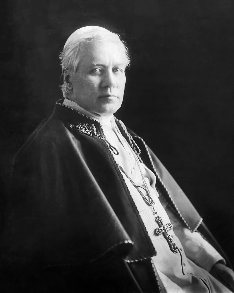 A photograph of Pope St. Pius X, seated, in white cassock with a pectoral cross.