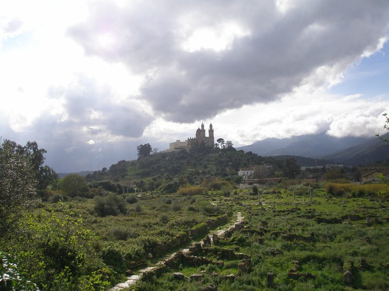 The ruins of ancient Hippo Regius near Annaba, Algeria, among green trees, with the Basilica of St. Augustine on the hill beyond.