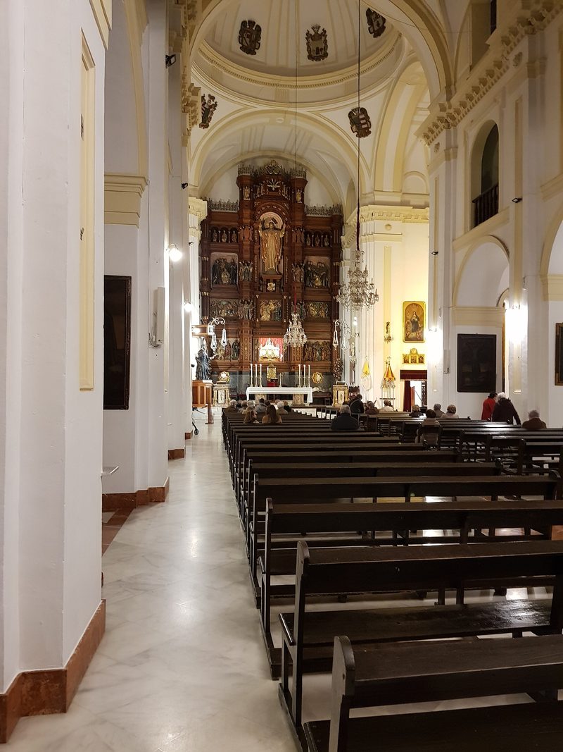 Inside the Basilica of St. John of Avila at Montilla: white walls, rows of pews and a gilded altarpiece.