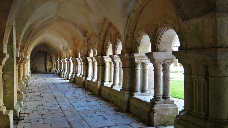 The Romanesque cloister of Fontenay Abbey in Burgundy: rounded arches and twin columns around a green garden.