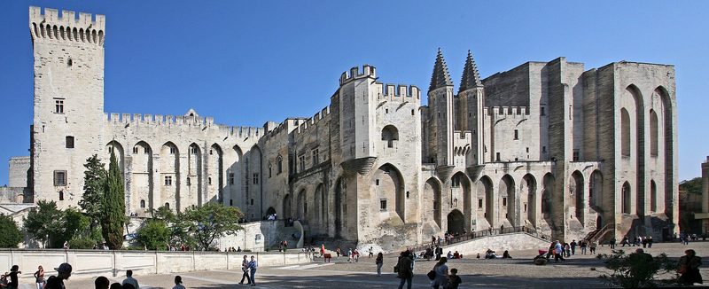The Palais des Papes in Avignon: massive Gothic towers and walls in pale stone under a blue sky.