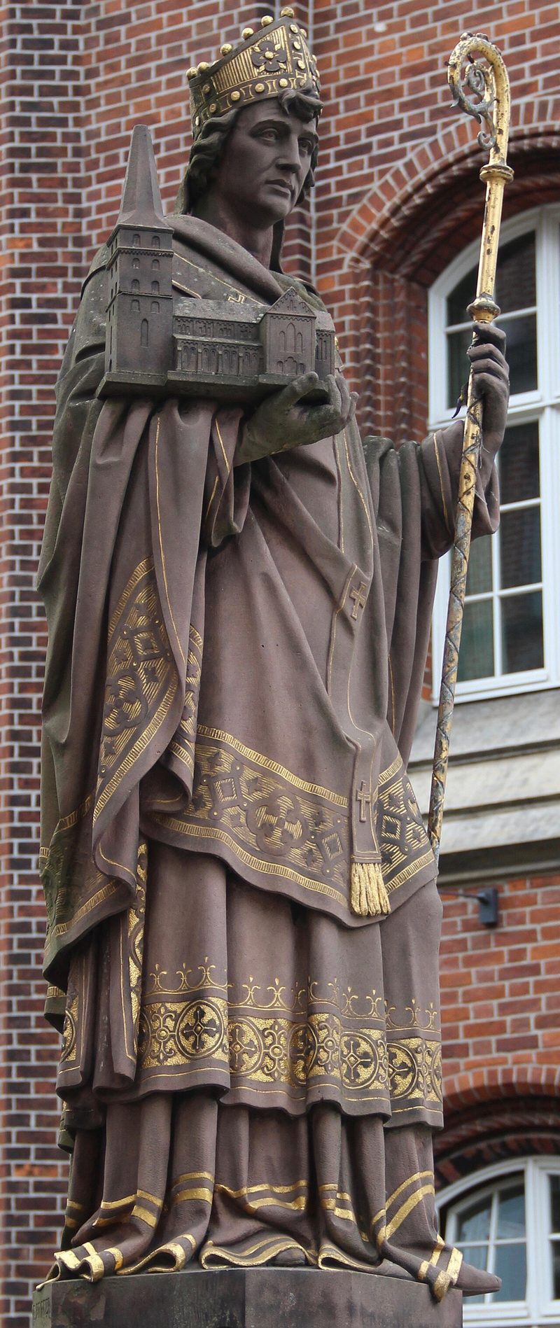 Stone statue of St. Ansgar as a bishop with a miter and crosier, against a brick building.