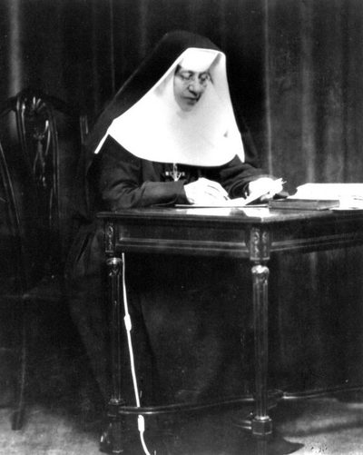 Black-and-white photograph of St. Katharine Drexel in a religious habit, writing at a desk.