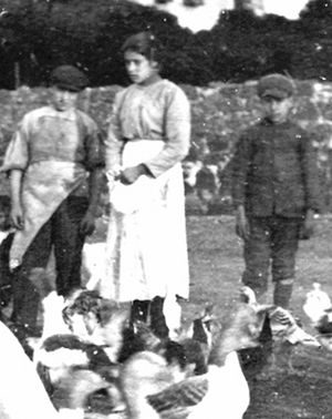 Old black-and-white photograph of a girl in an apron standing outdoors between a man and a boy.