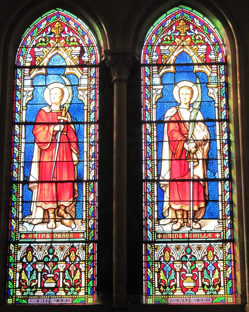 Two stained-glass windows, each showing a saint in a red cloak holding a palm.
