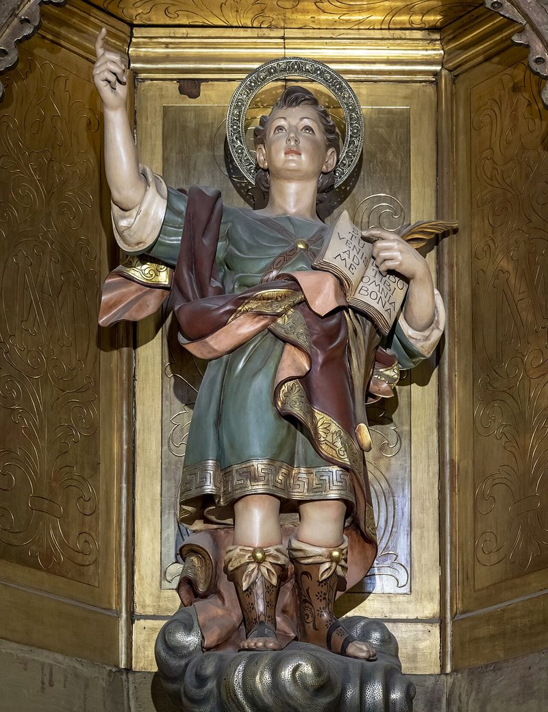 Painted statue of St. Pancras as a boy with a halo, holding a palm and a book.